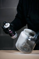 Pormenor de utilizador a aplicar o Spray MTN Multi-Surface Primer da marca Montana Colors num frasco de vidro.