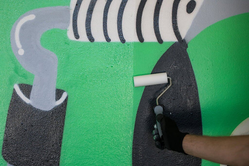 Pormenor de utilizador a aplicar com um rolo o MTN Mural Varnish Protection sobre um graffiti.