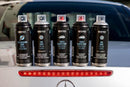 Vários sprays da coleção de tinta automóvel da marca Montana Colors, pousadas sobre a bagageira de uma Mercedes branco.