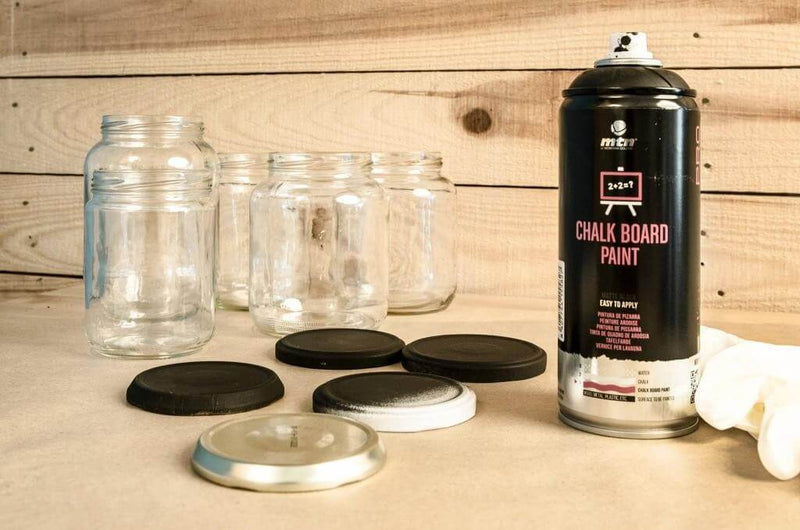 Lata de spray de tinta lousa junto a um conjunto de tampas de recipientes de vidro devidamente pulverizadas.