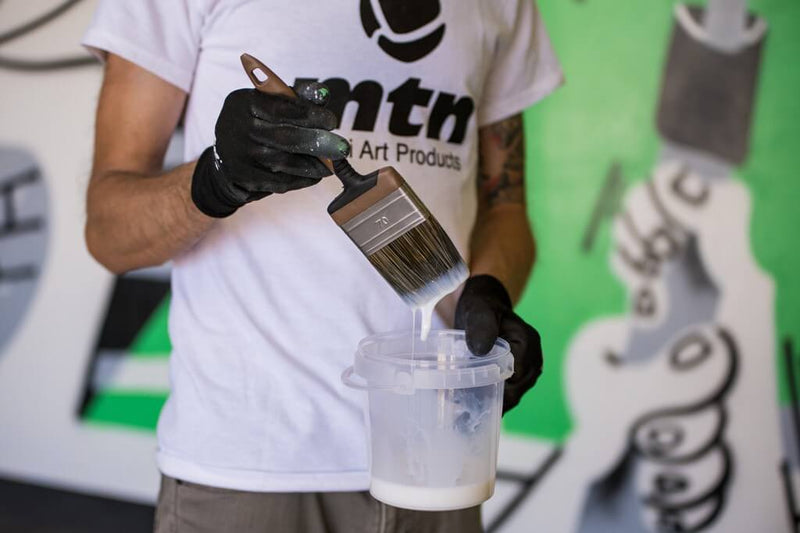 Artista a molhar uma trincha no verniz protetor para murais da marca Montana Colors.